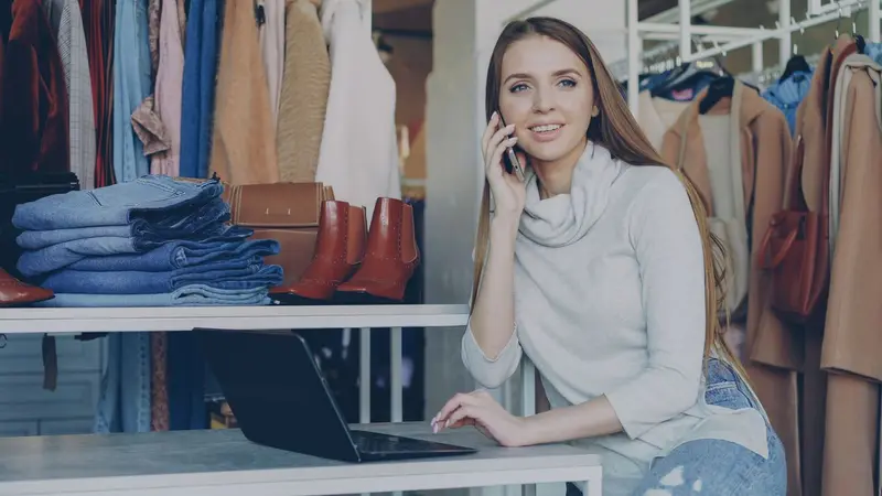 Vendedora atendiendo un pedido por teléfono en su boutique mientras vende por internet
